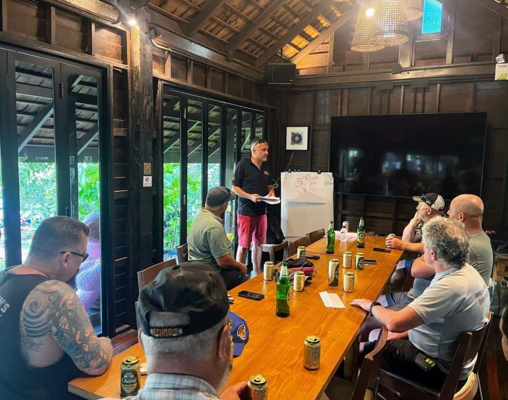 A group of motorcycle tour participants attending a briefing session with the guide at a wooden meeting room in Thailand