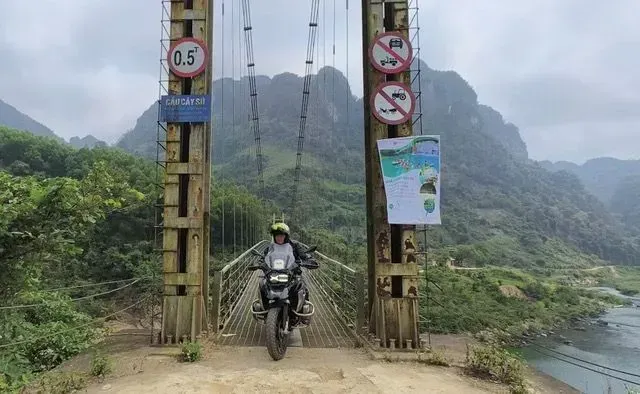 Adventure motorcyclist crossing suspension bridge in remote Laos mountains