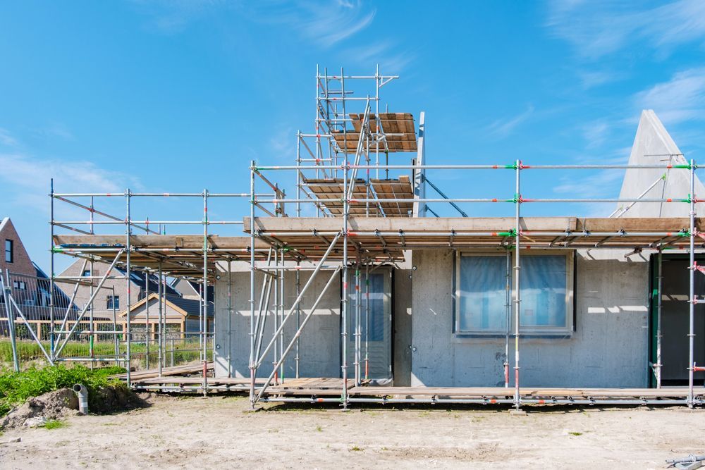 Casa in costruzione con impalcature e tetto parzialmente finito sotto un cielo azzurro