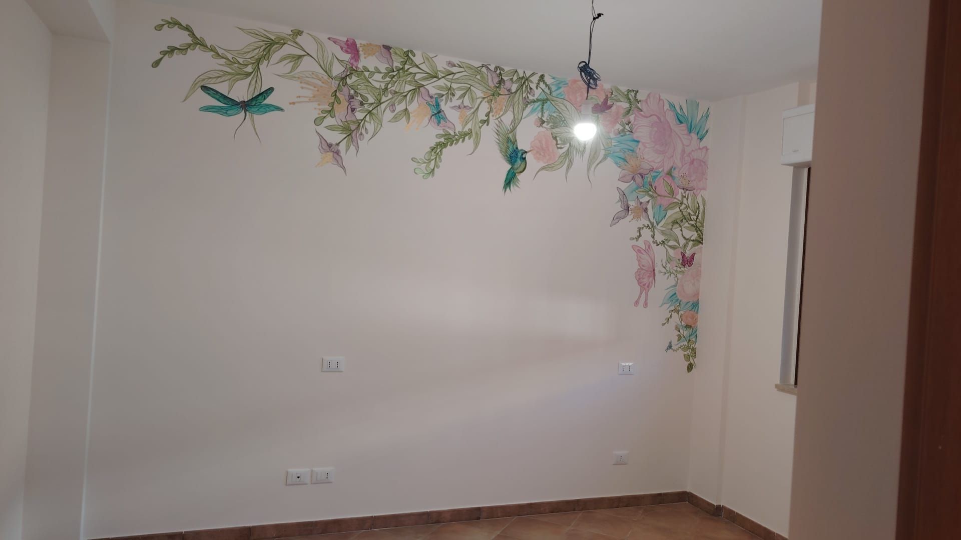 Stanza bianca vuota con un bordo decorativo floreale vicino al soffitto e una lampadina sospesa.