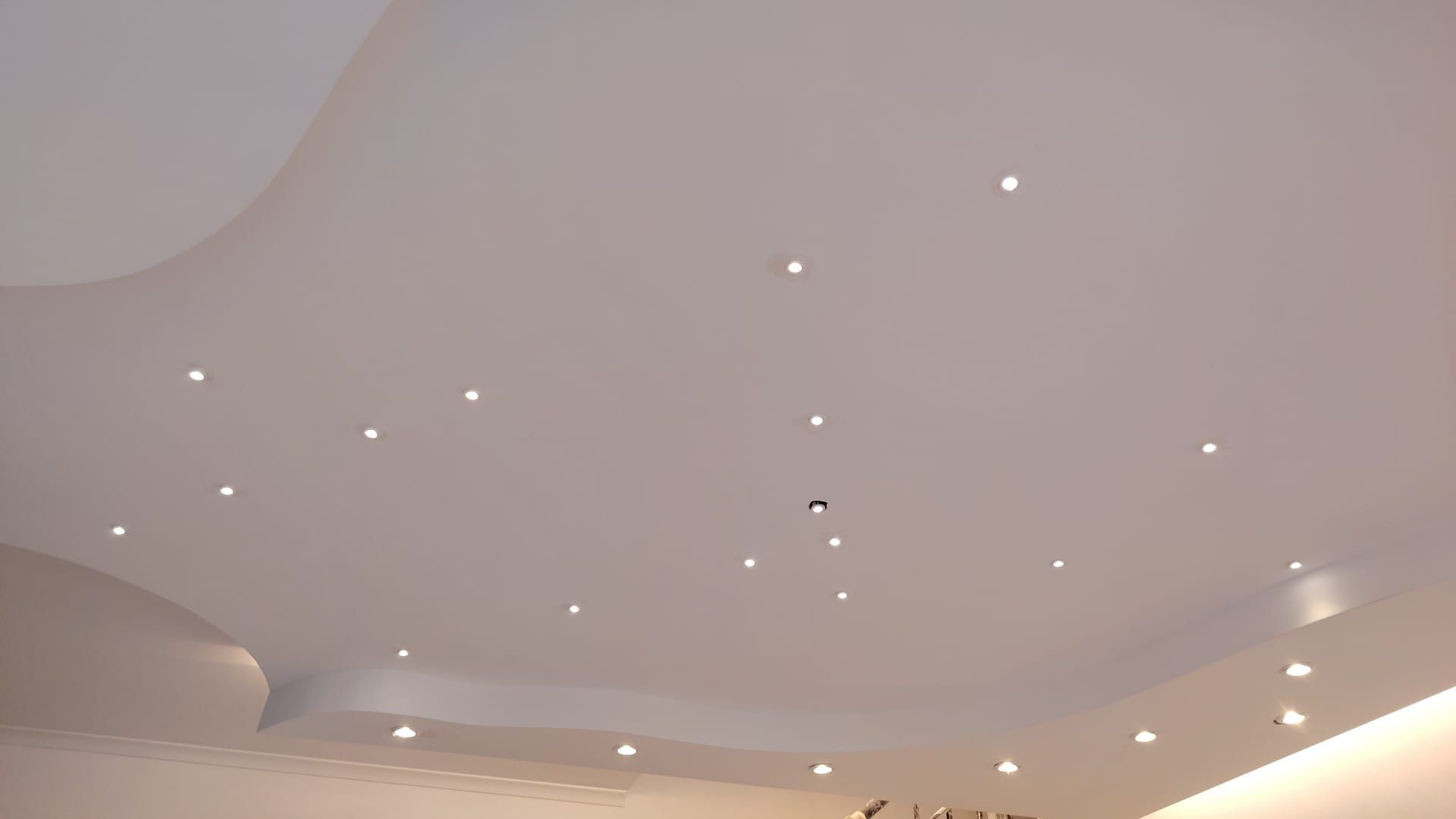 Soffitto con piccoli faretti a incasso e modanature curve in una stanza moderna.