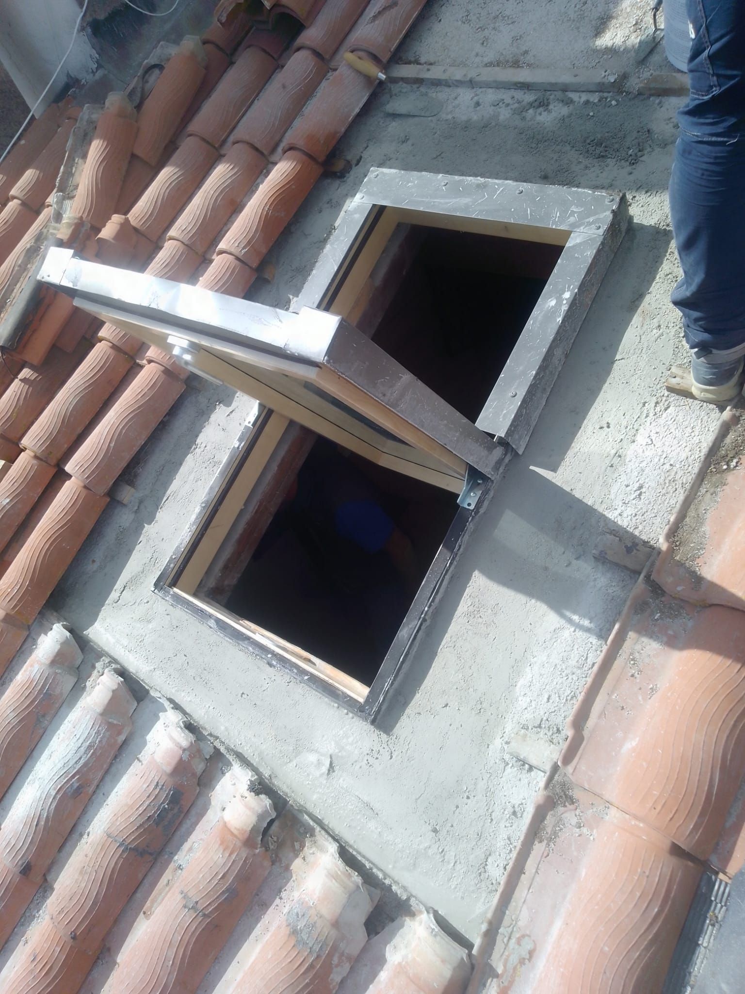 Un portello aperto sul tetto di tegole rosse, con una scala, lascia intravedere un interno buio sottostante.