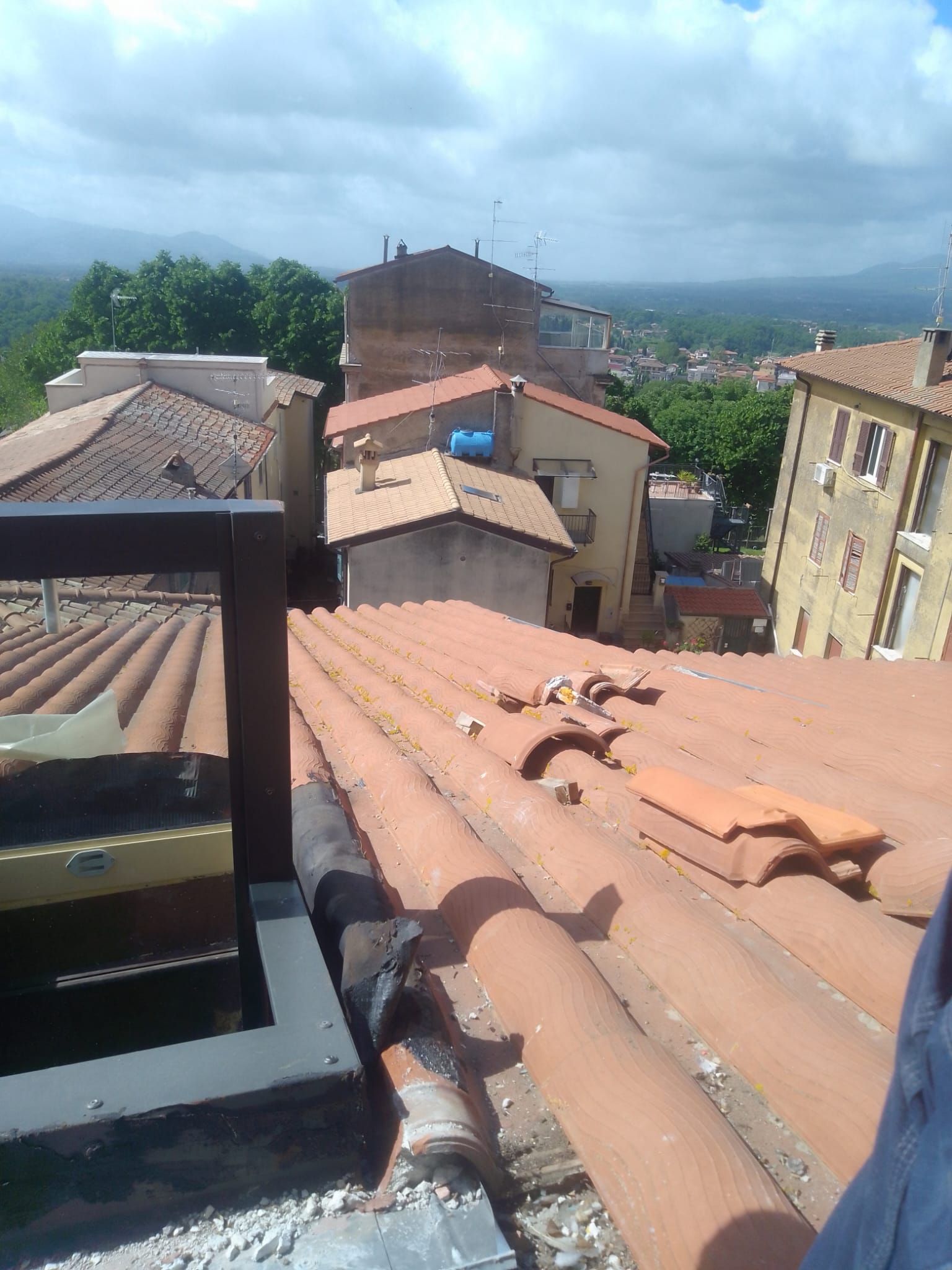 Vista dai tetti di edifici con tegole in terracotta sotto un cielo nuvoloso, con colline sullo sfondo.