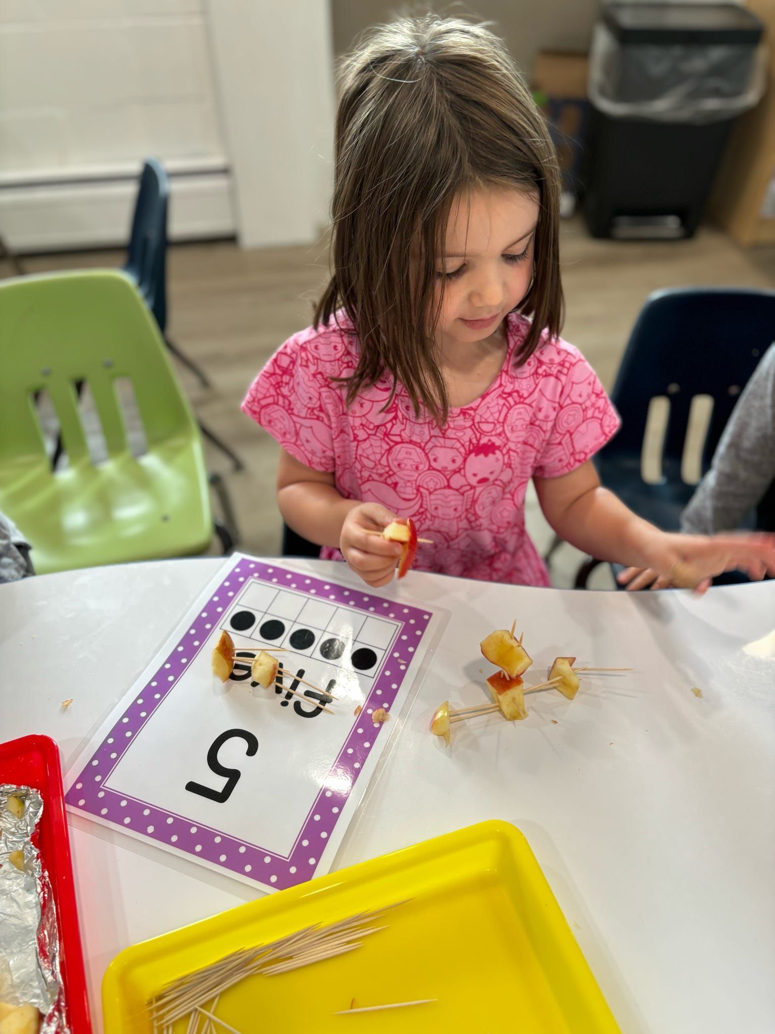 A little girl is sitting at a table playing with food.