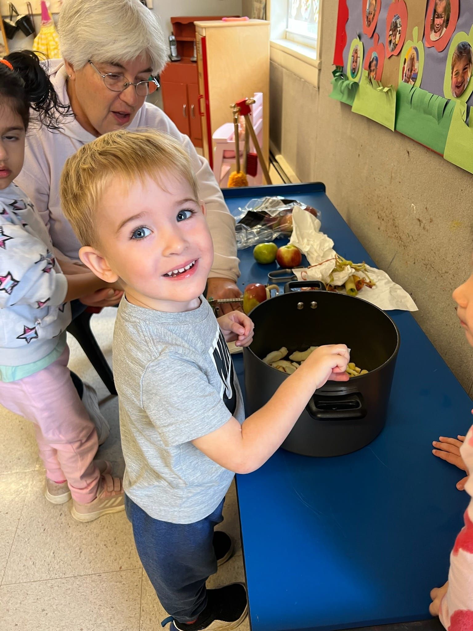 A little boy is standing in front of a pot of food.