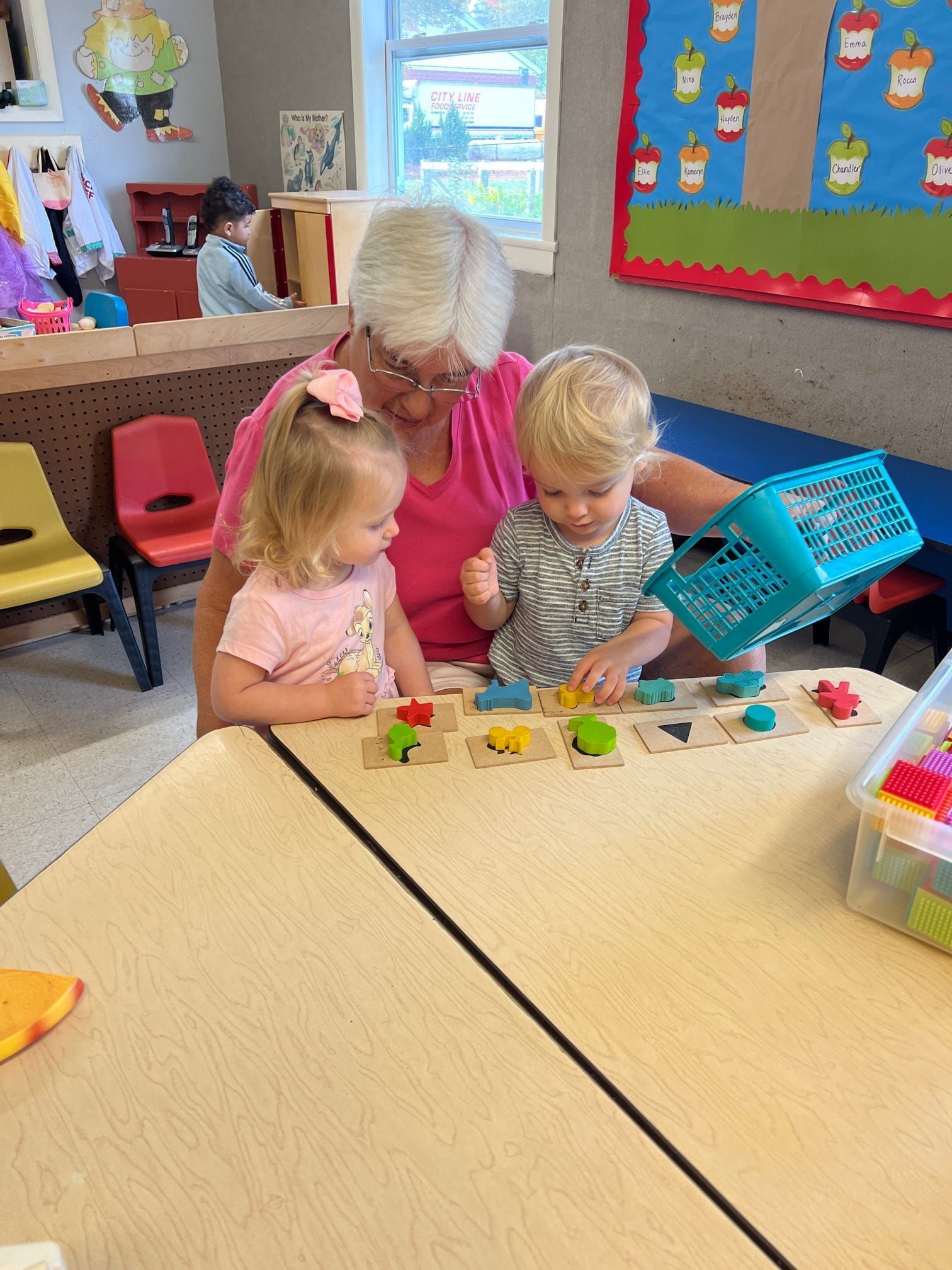 A woman is sitting at a table with two children playing with toys.