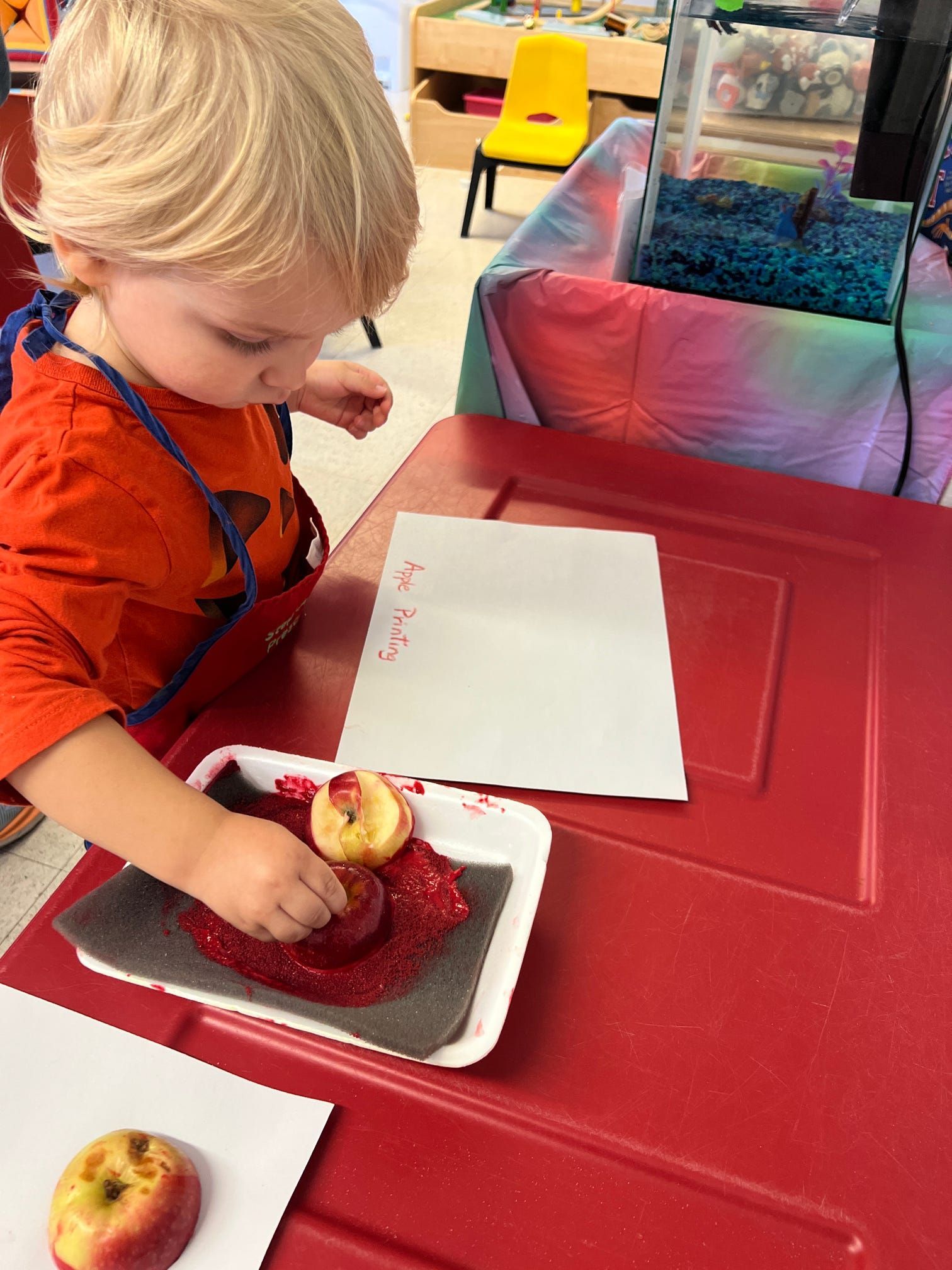 A young boy is painting an apple with red paint.