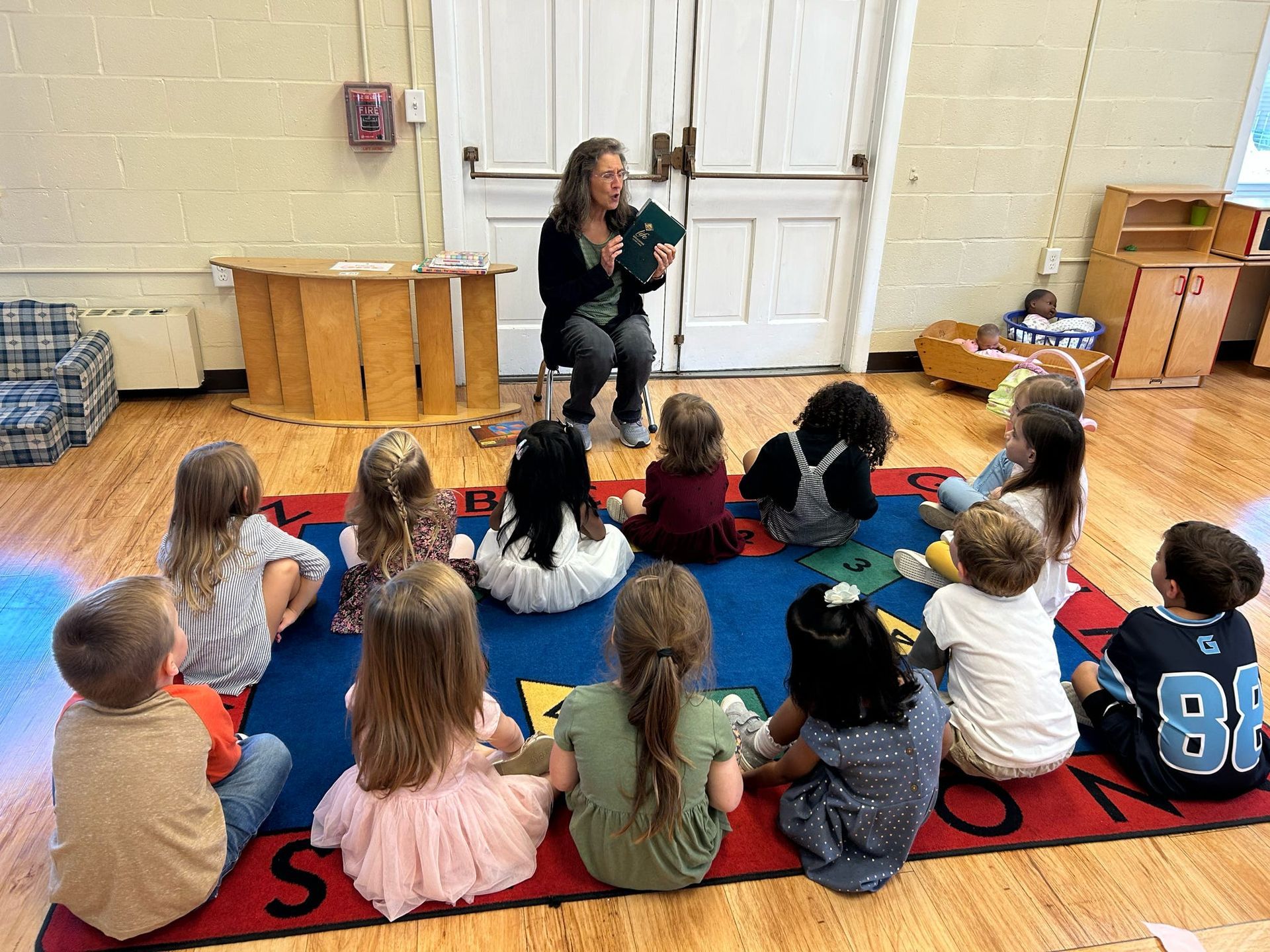 A woman is reading a book to a group of children sitting on the floor.