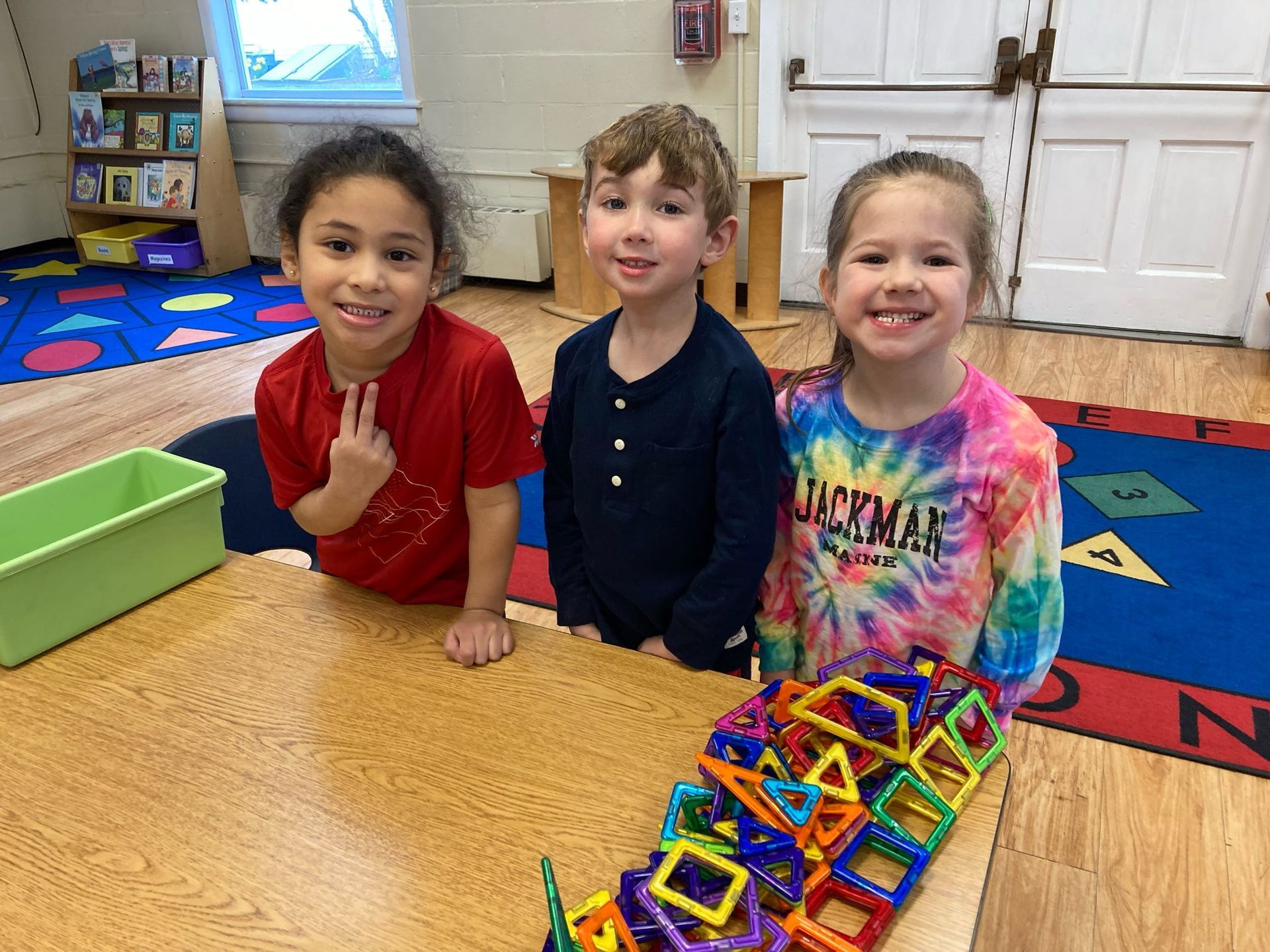 Three children are sitting at a table with magnetic blocks.