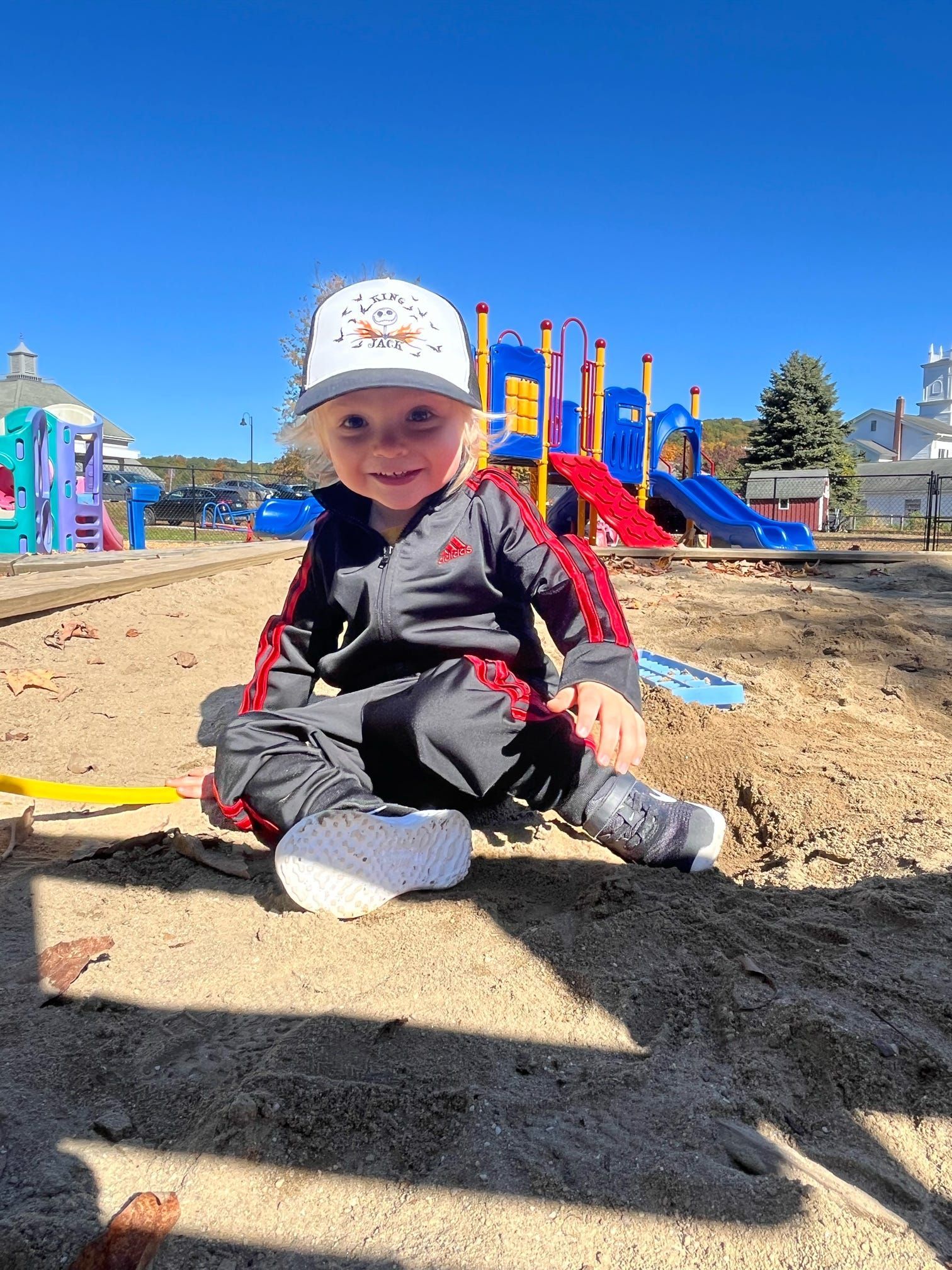A little boy is sitting in the sand at a playground.