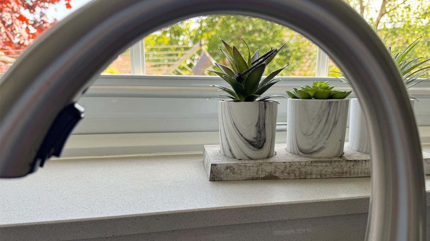 Two potted plants are sitting on a kitchen window sill with tap