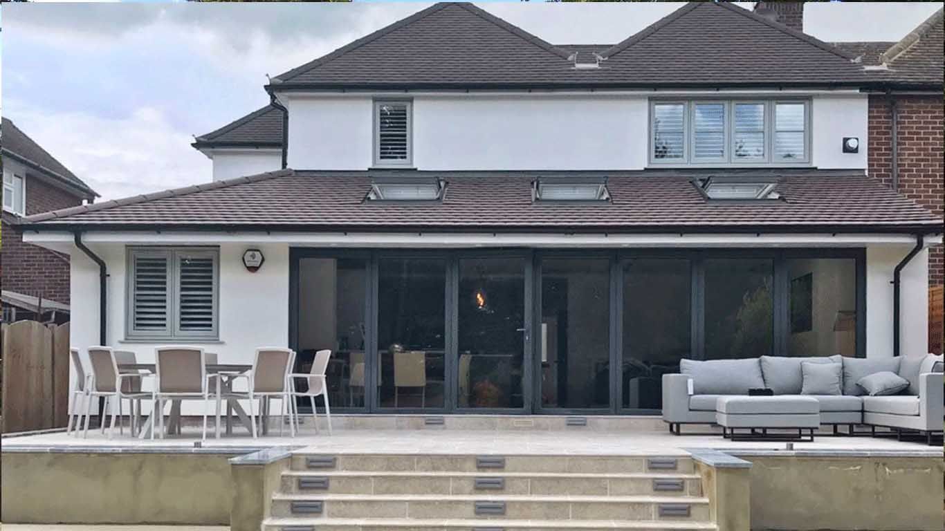 The back of a house with bifolding doors and a patio area and a dining table and chairs.