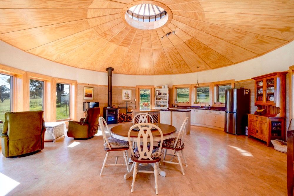 Spacious round living room with wood ceiling, large windows, fireplace, and dining table in the center