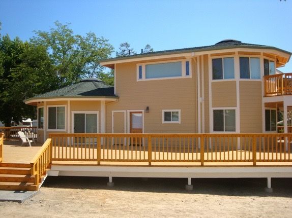 Tan house with a yellow ramp and deck, featuring a screened porch and two-story section under a blue sky
