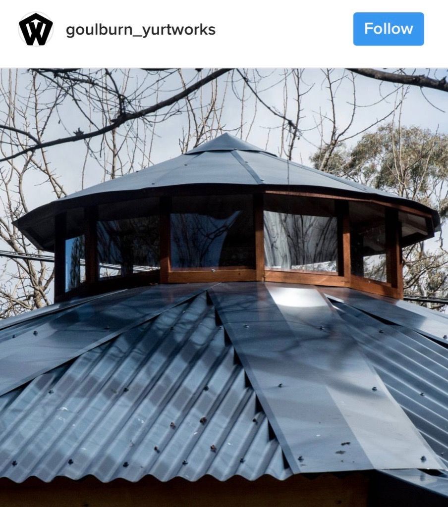 Octagonal metal-roofed gazebo with black corrugated panels and wood-framed windows among bare tree branches