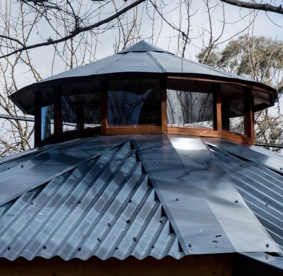 Round metal-roofed wooden pavilion among bare trees in winter