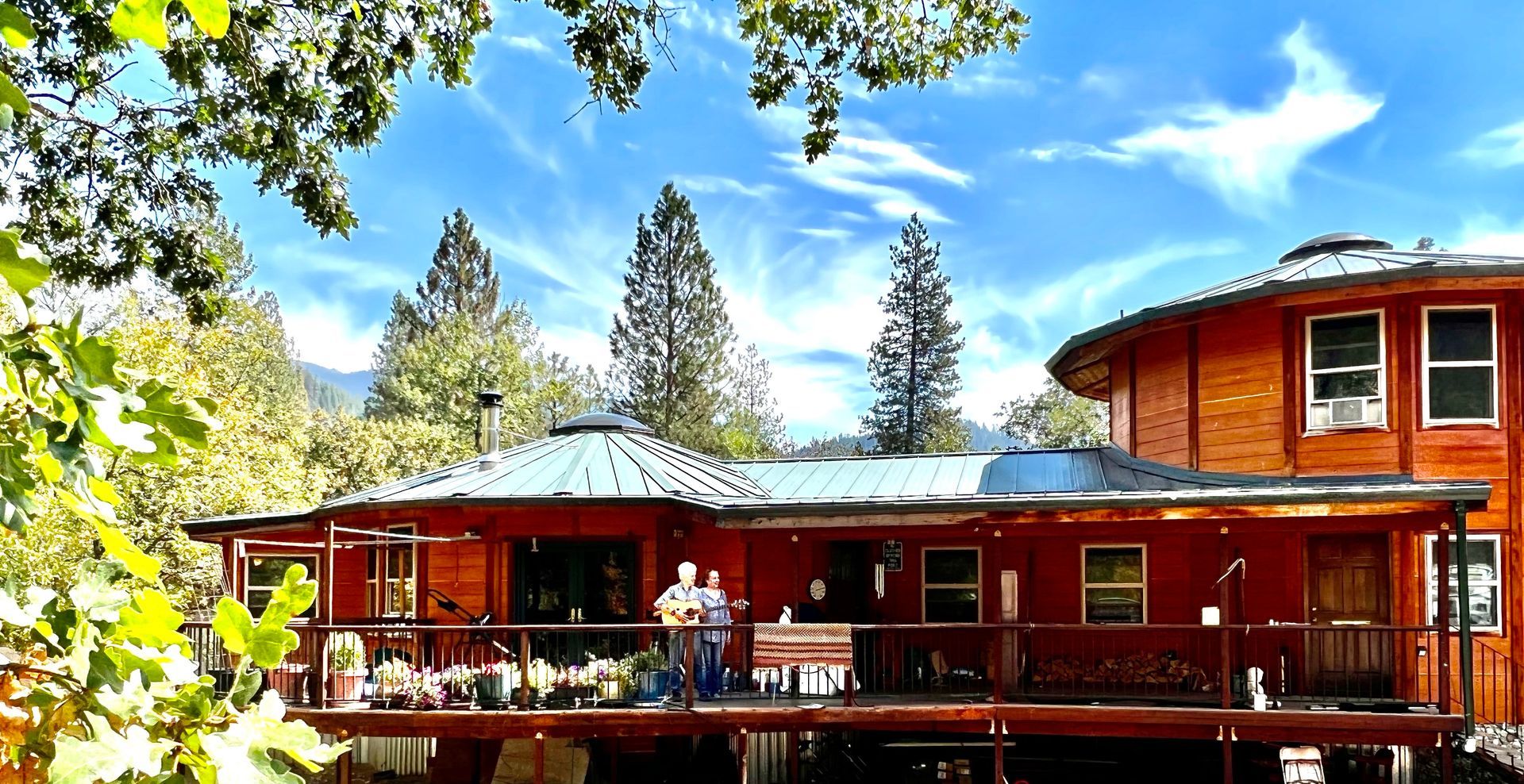 Red cabin-style house with a porch and large windows among tall pine trees