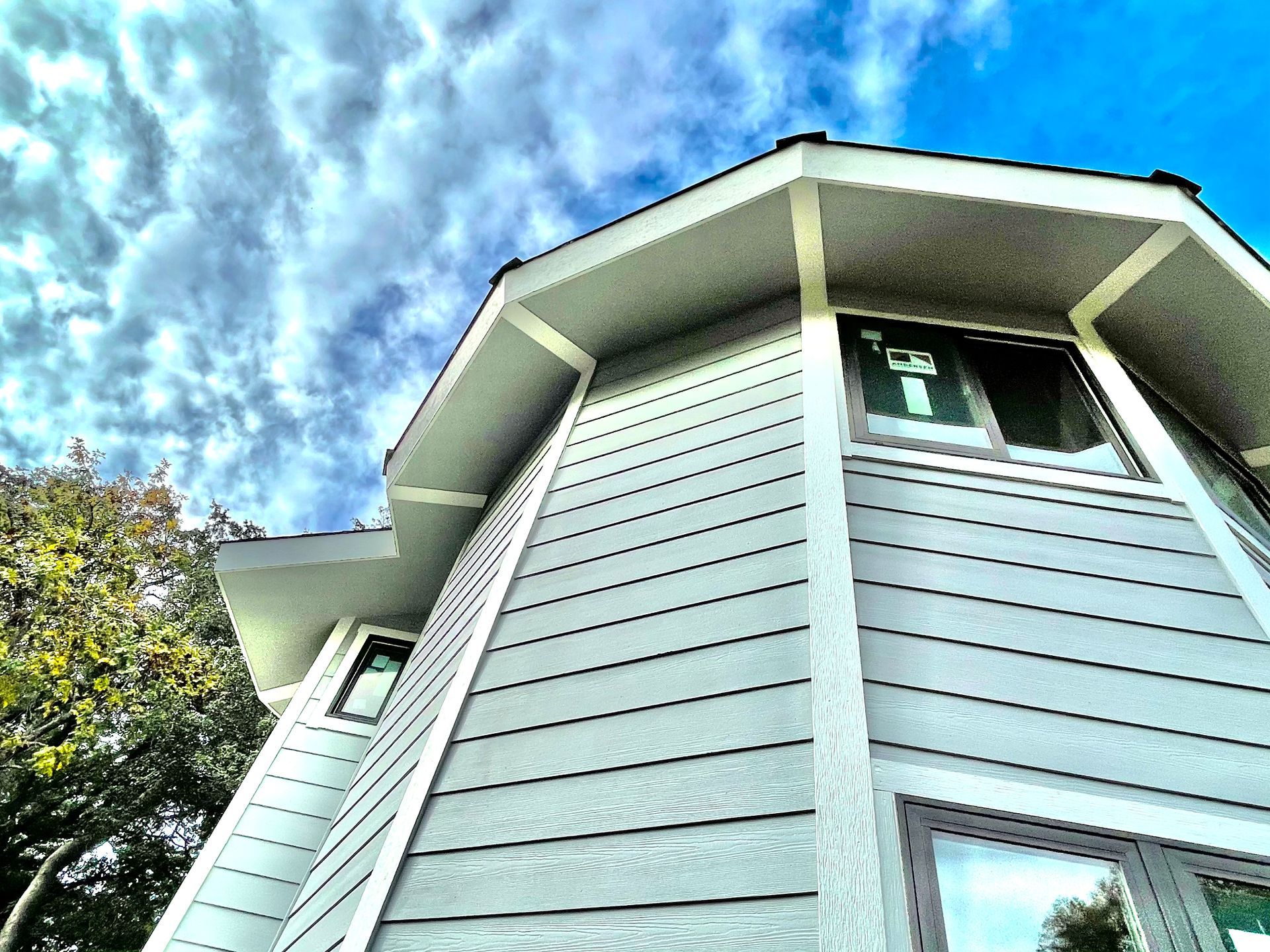 Low-angle view of a light blue house exterior with white trim against a cloudy sky
