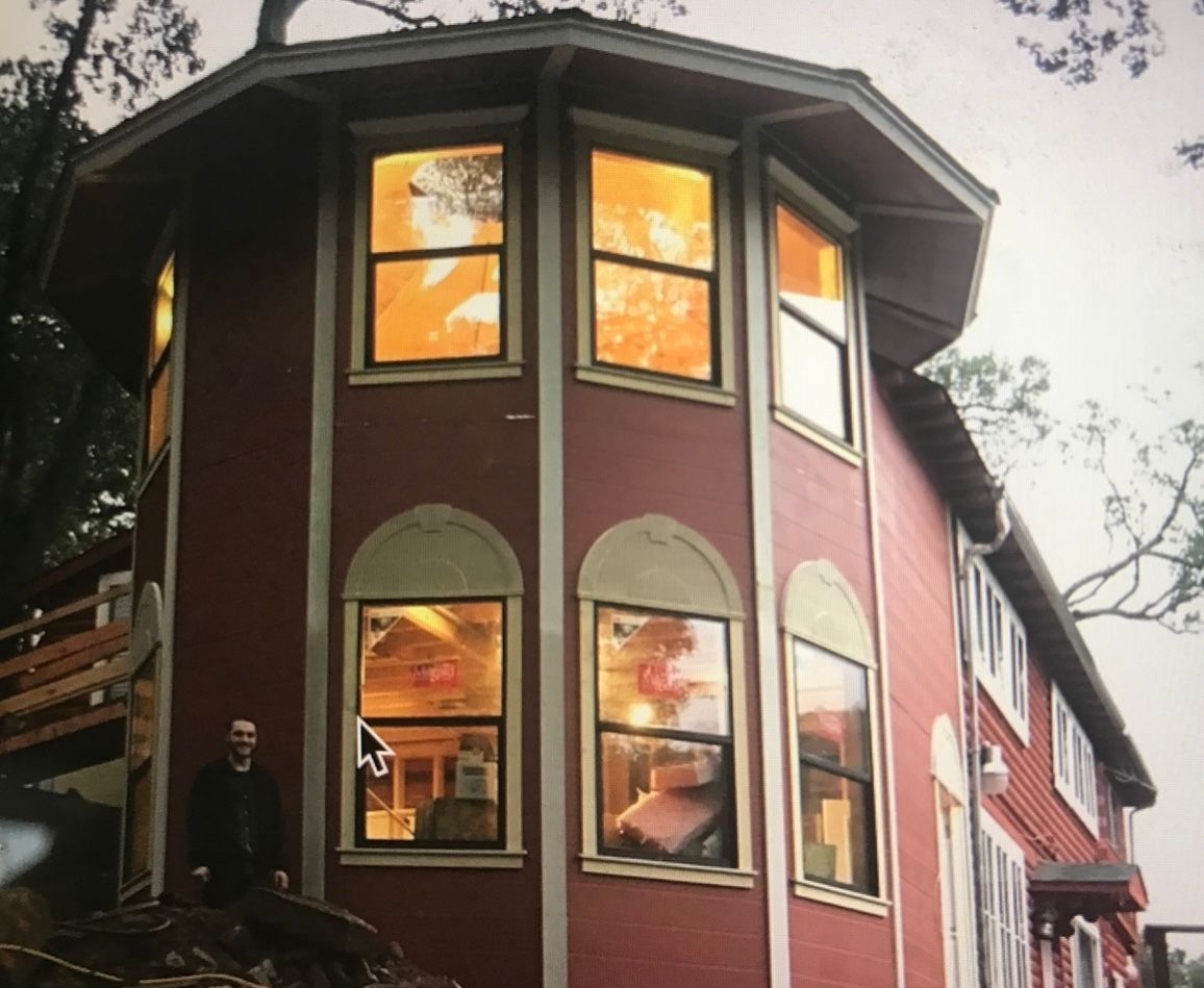 Red octagonal house with lit windows at dusk, seen from below through tree branches