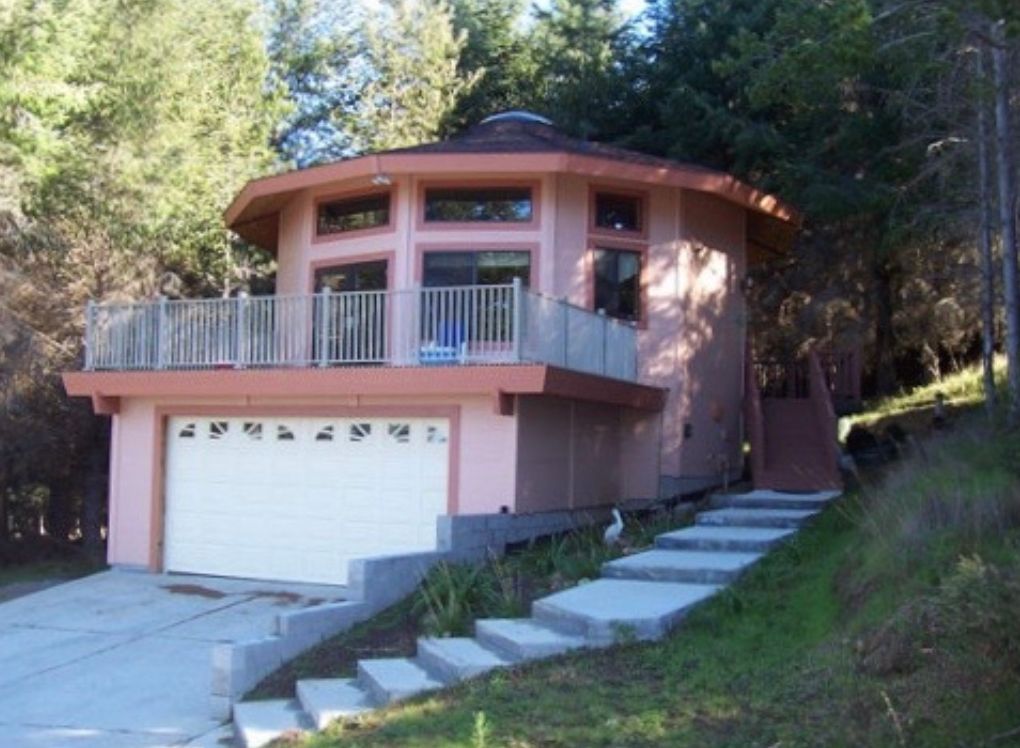 Pink two-story house with a garage, balcony, and stairs on a wooded hillside