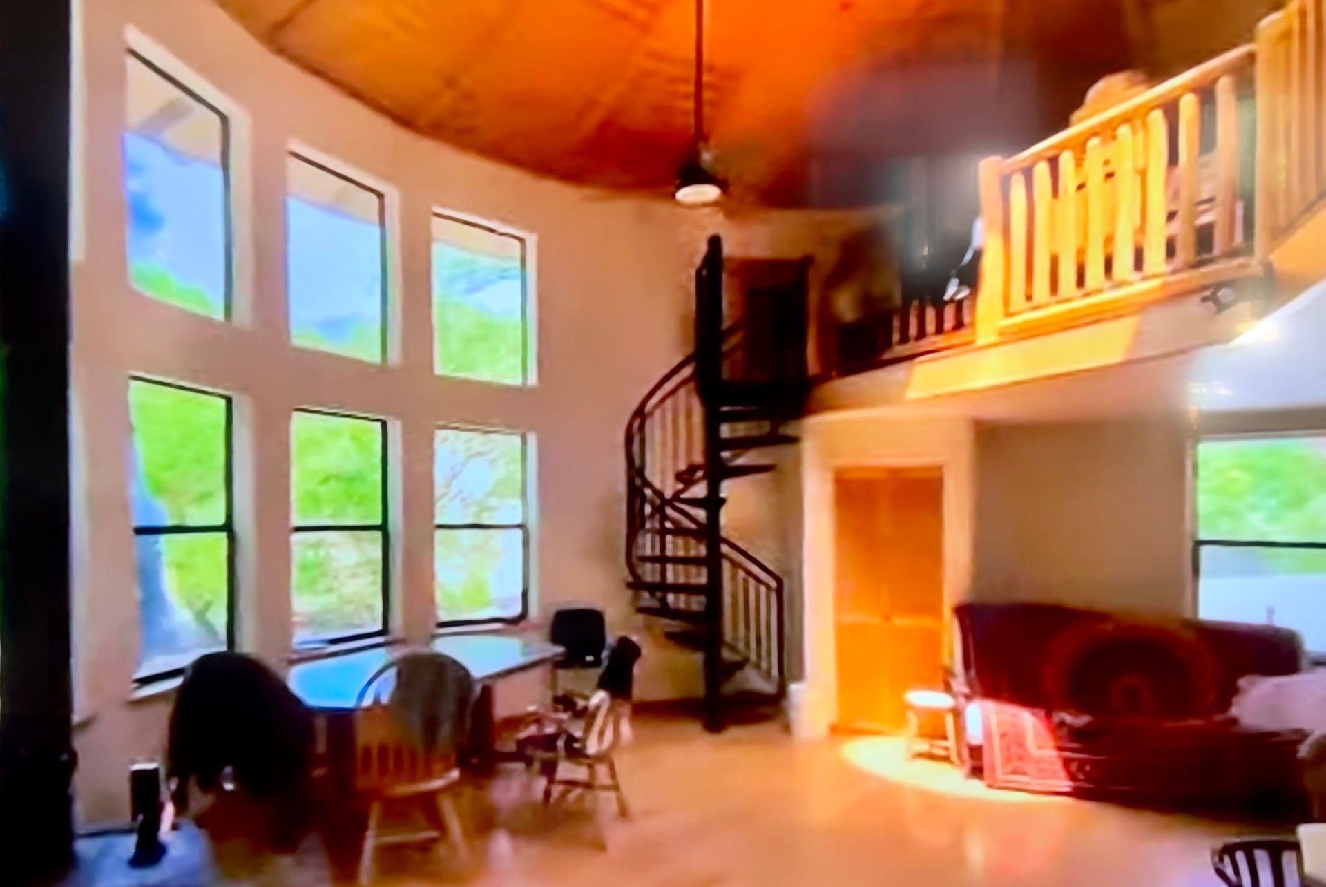Bright living room with tall windows, spiral staircase, loft balcony, and red sofa
