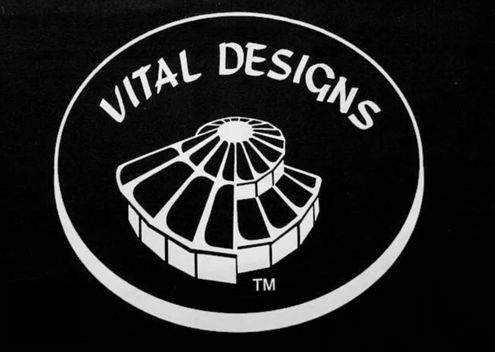 Vital Designs logo with white spiral emblem and text on a black oval background