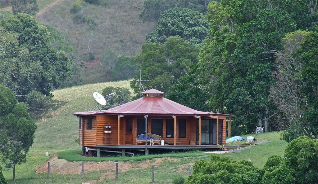 Small wooden cabin with a red roof in a lush green rural hillside landscape