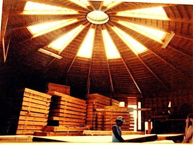 Wooden interior with stacked lumber and a person standing under a bright circular skylight.