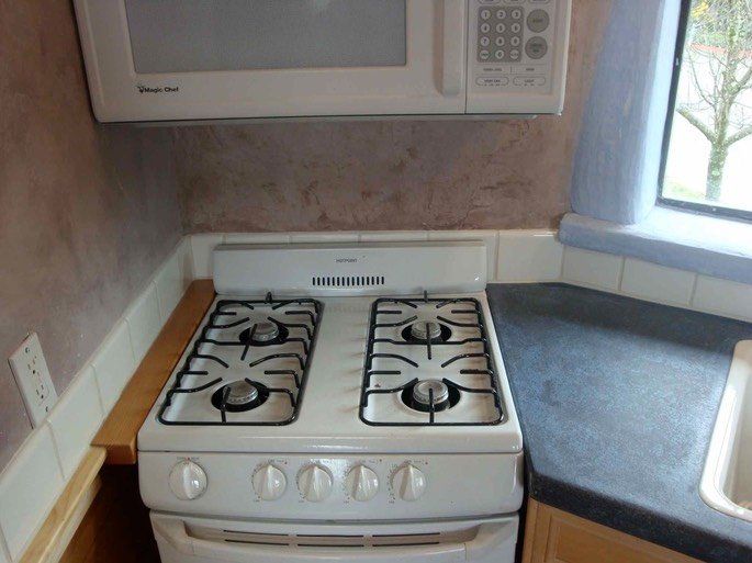 Small kitchen with white gas stove, gray countertop, microwave, and a window.