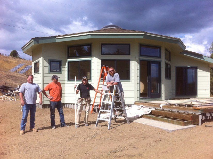 Four people working outside a partially built house with a ladder and construction materials