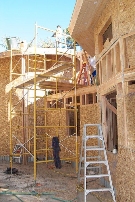 Construction scaffolding beside a wooden house exterior, with ladders and tools on site