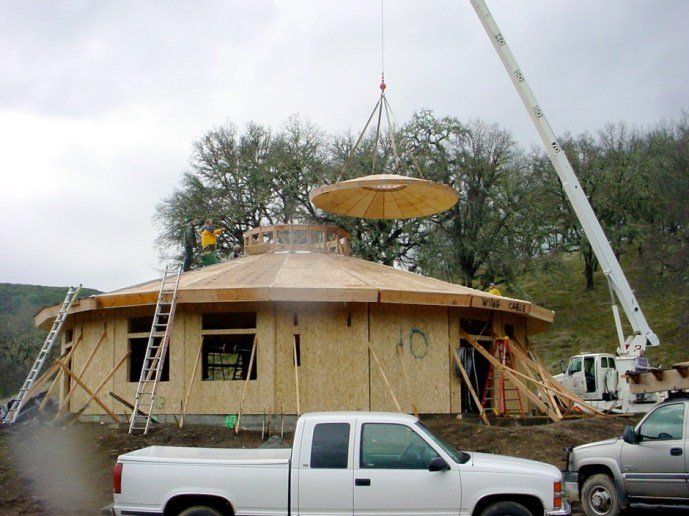 House under construction with a crane lifting a round roof piece over a pickup truck