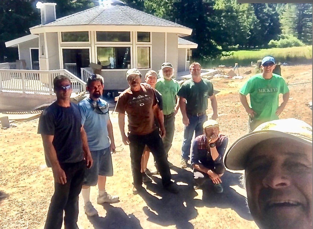 Group of people standing outdoors in front of a small building, with one person taking a selfie in the foreground