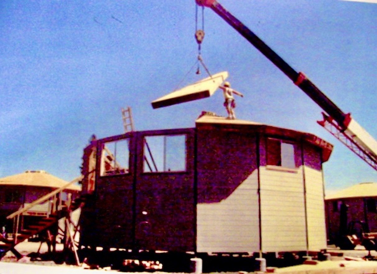 Crane lifting a small modular house onto a foundation at a construction site.