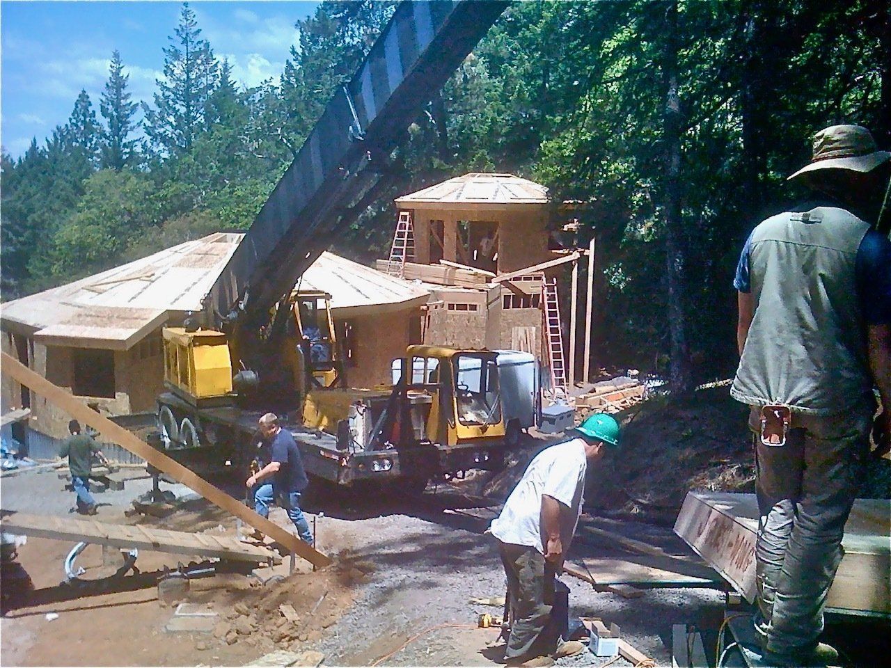 Construction workers moving a house with a crane in a wooded area