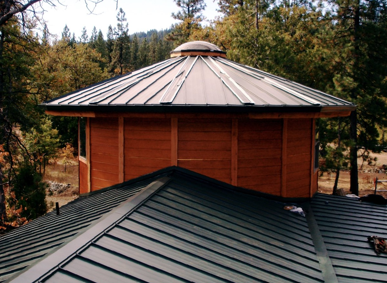 Octagonal wooden roofed structure with green metal roof panels in a wooded area