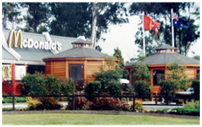 McDonald’s restaurant with wooden huts, trees, flags, and a red-and-white building sign