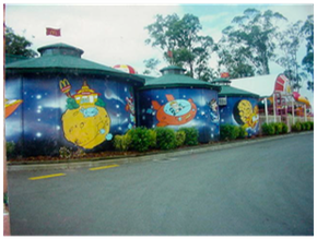 Colorful cartoon murals on curved building walls beside a quiet road under trees