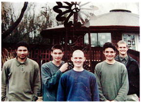 Five people standing outdoors in front of a round building and windmill structure