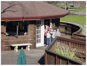 People standing outside a small brick pavilion with a curved wooden deck and railing