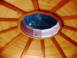 Interior view of a wooden dome ceiling with an octagonal skylight showing the night sky