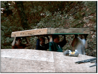 Workers lifting a wooden beam under a partially built roof outdoors