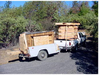 Two small white utility trailers loaded with wooden crates on a road by trees