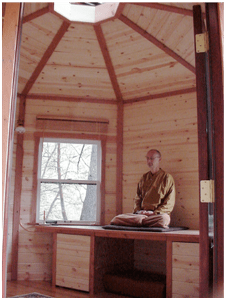 Person seated inside a small wooden cabin with a window and built-in bench seating.