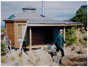 Person in hard hat walking beside a small wooden house under construction outdoors
