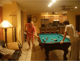 Two people playing pool in a warmly lit living room with a billiards table.