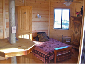 Wooden cabin bedroom with bed, window, door, and rustic furniture