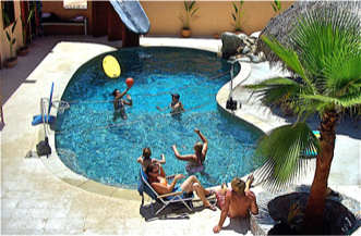 People relaxing in a backyard pool with lounge chairs, palm trees, and a bright yellow float.