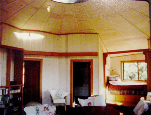 Cozy room with high ceiling, cream walls, wooden trim, and chairs near a window and fireplace.
