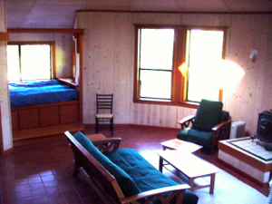 Small living room with teal chairs, a coffee table, window seat, and bright sunlight